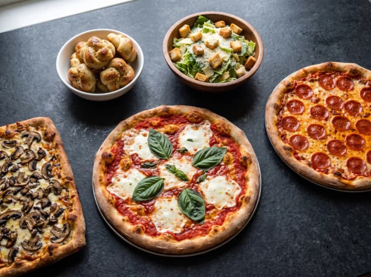 Pizzas, garlic knots, and salad on a charcoal table